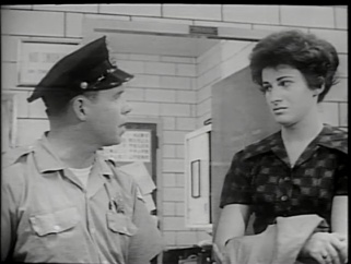 A policeman speaks with a young woman in a police station.